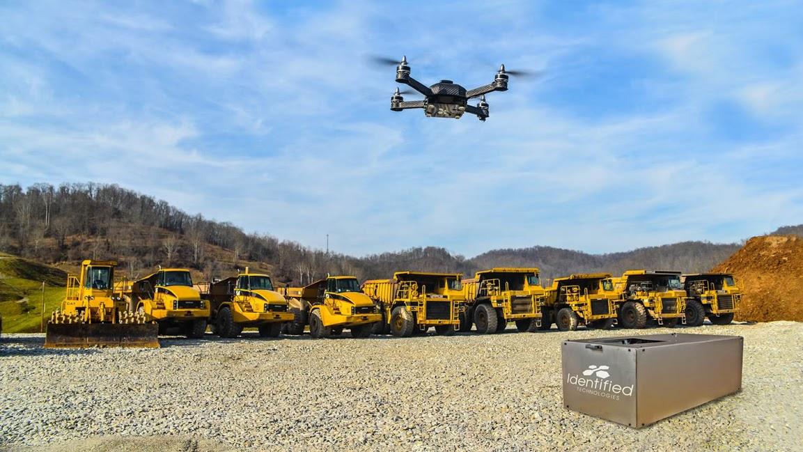 Drone hovering above a fleet of mining haul trucks and heavy equipment, with an Identified Technologies base station in the foreground